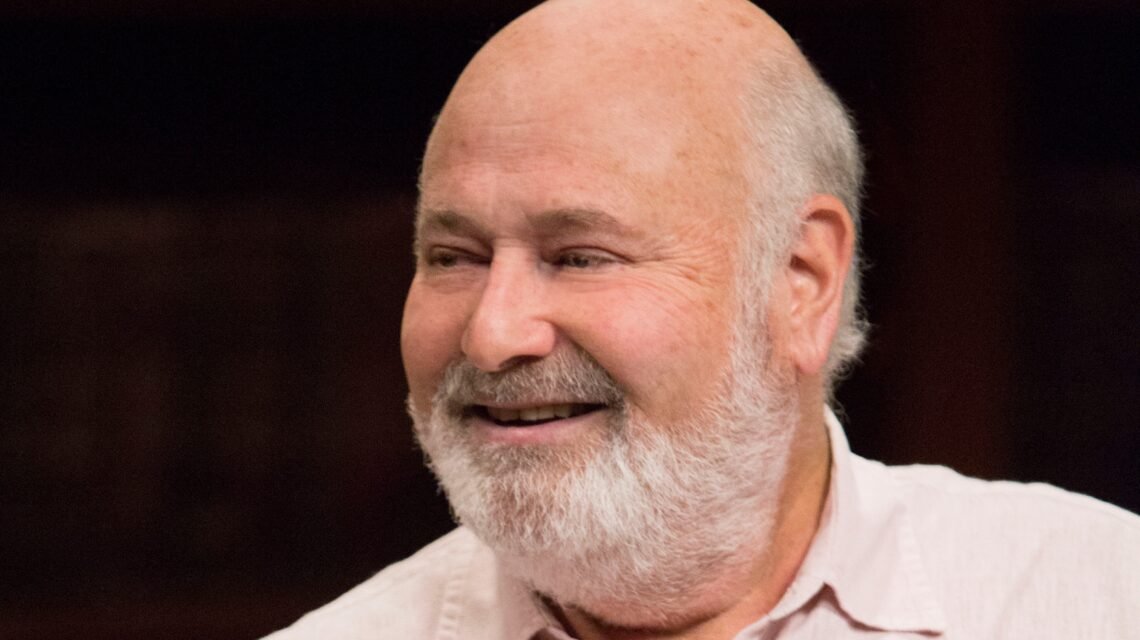 Rob Reiner smiling in a light-colored shirt against a dark background – Hollywood director and actor known for classics like When Harry Met Sally and A Few Good Men.