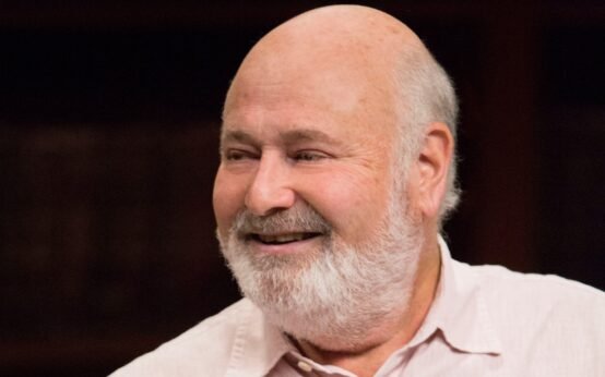 Rob Reiner smiling in a light-colored shirt against a dark background – Hollywood director and actor known for classics like When Harry Met Sally and A Few Good Men.